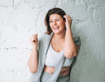 Beautiful happy emotional brunette young woman plus size body positive in comfortable sport wear near the white brick wall